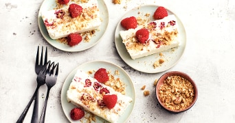 Plakjes vanille-ijstaart met verse frambozen en kruimels op borden.