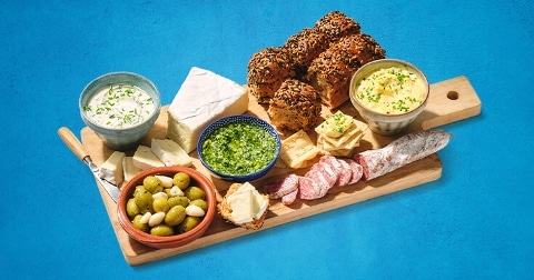 Borrelplank met diverse kazen, salami, olijven, dips en broodjes op een houten plank.