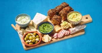 Borrelplank met diverse kazen, salami, olijven, dips en broodjes op een houten plank.