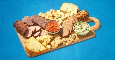 Tapasplank met verschillende kazen, vleeswaren, crackers en dips op een houten snijplank.