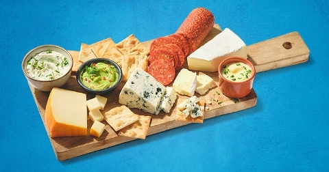 Borrelplank met verschillende kazen, crackers, dips en vleeswaren, inclusief blauwe kaas en brie.