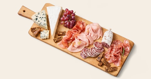 Borrelplank met verschillende soorten kaas, vleeswaren, druiven en stukjes toast op een houten serveerplank.