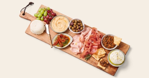 Borrelplank met diverse Italiaanse vleeswaren, kazen, tapenade, hummus, olijven, zongedroogde tomaten, druiven en crackers.
