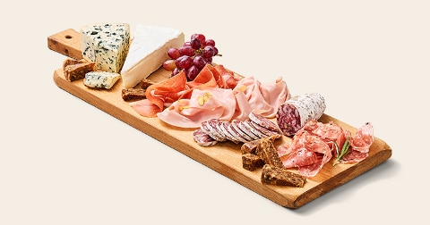 Borrelplank met verschillende soorten vleeswaren, kaas, druiven en stukjes brood op een houten plank.