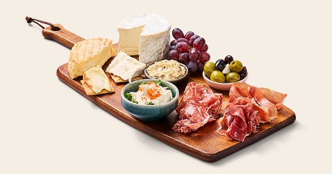 Luxe borrelplank met verschillende soorten kaas, charcuterie, druiven, olijven en dips op een houten serveerplank.