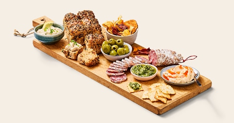 Borrelplank met brood, olijven, chips, smeersels, crackers, pesto en verschillende soorten worst.