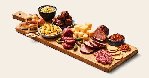 Borrelplank met verschillende hapjes zoals mini worstenbroodjes, blokjes kaas, gehaktballetjes, schijfjes worst, augurken, ananasstukjes, toastjes, crackers en dips.