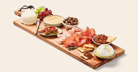 Borrelplank met diverse Italiaanse vleeswaren, kazen, tapenade, hummus, olijven, zongedroogde tomaten, druiven en crackers.