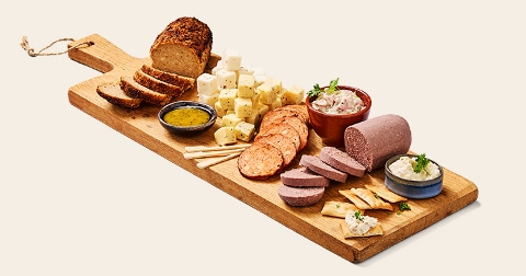 Borrelplank met verschillende soorten vleeswaren, kaasblokjes, dips en brood op een houten serveerplank.