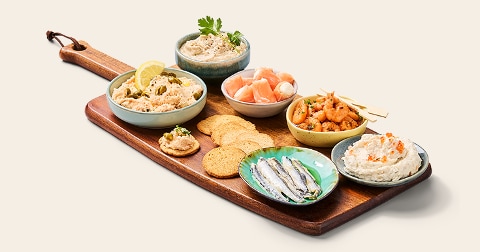 Borrelplank met verschillende visdelicatessen, waaronder toastjes, zalm, garnalen, haringfilets en diverse vismousse in kommetjes.