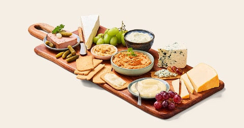 Borrelplank met verschillende kazen, druiven, toast, dips, crackers, groene druiven en augurken.