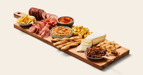 Borrelplank met diverse vleeswaren, kaasblokjes, brie, dipjes, chips, grissini en toast op een houten serveerplank.