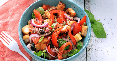 Salade met stukjes brood, tomaat, rode ui, olijven, kappertjes en basilicum in een blauwe kom