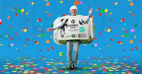 Persoon verkleed als AH scharreleieren doos op een blauwe achtergrond met gekleurde confetti