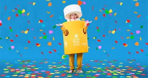 Persoon verkleed als fles AH Ginger Power tussen vallende confetti op blauwe achtergrond