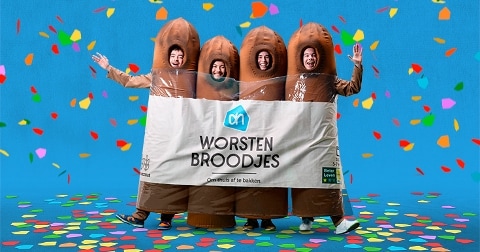 Gezellige carnavalsoutfits in de vorm van worstenbroodjes met Albert Heijn-logo, kleurrijke confetti op blauwe achtergrond