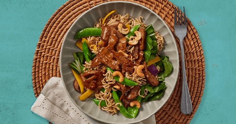 Gebakken noedels met stukjes rundvlees, peultjes, gele paprika, spinazie en cashewnoten op een bord