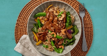 Gebakken noedels met stukjes rundvlees, peultjes, gele paprika, spinazie en cashewnoten op een bord