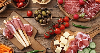 Tapasplank met diverse soorten vleeswaren, kaasblokjes, olijven, tomaatjes en groentesticks op een houten tafel