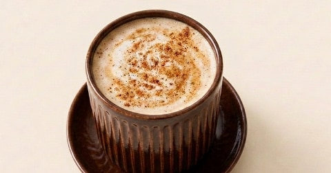 Kopje cappuccino met melkschuim en kaneel, geserveerd in een bruine mok op een schoteltje.
