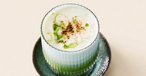 Glas matcha latte met melkschuim en een vleugje kaneel, geserveerd op een schoteltje.