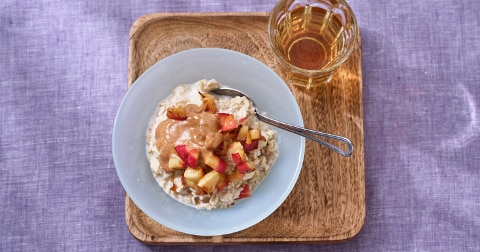 Havermoutpap met stukjes appel en pindakaas in een kom, geserveerd op een houten dienblad met een glas appelsap