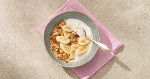 Kom met yoghurt, muesli en plakjes banaan op een roze servet