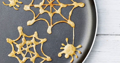 Spinnenwebvormige pannenkoekenbeslag in een koekenpan op een witte houten ondergrond