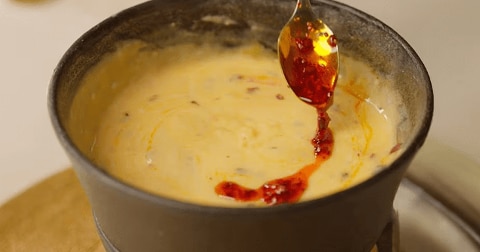Pan met gesmolten kaasdip en een lepel met chilisaus erboven