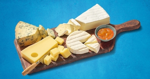 Diverse selectie van kazen met een potje jam op een houten serveerplank.