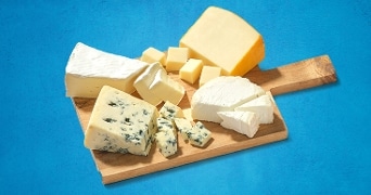 Verschillende soorten kaas op een houten plank, waaronder brie, blauwe kaas en jong belegen kaas.