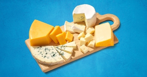 Verschillende soorten kaas op een snijplank, inclusief blauwe kaas, camembert en cheddarkaas.