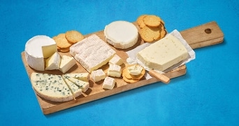 Kaasplank met verschillende soorten kaas zoals brie, blauwe kaas en camembert, vergezeld van crackers, op een houten snijplank.