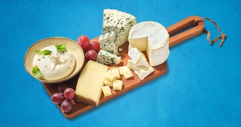 Assortiment van kazen met dip en druiven op een houten plank.