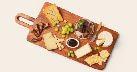 Borrelplank met verschillende kazen, druiven, stukjes vlees, chocoladedessert, blauwe bessen en jam.