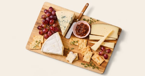 Kaasplank met verschillende soorten kaas, druiven, crackers, vijgenjam en verse tijm op een houten serveerplank.