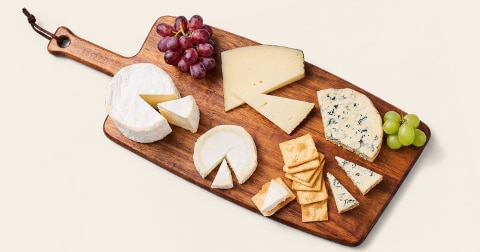 Verschillende soorten kaas, druiven en crackers op een houten serveerplank.
