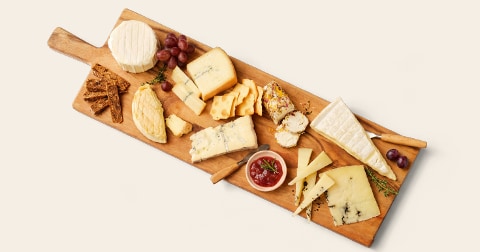 Kaasplank met verschillende soorten kaas, druiven, crackers en een kom met chutney op een houten serveerplank.