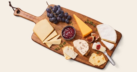 Borrelplank met verschillende soorten kaas, blauwe druiven, vijgen, crackers, takjes tijm en een schaaltje met rode jam.