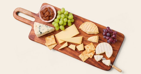 Kaasplank met verschillende soorten kaas, crackers, groene en rode druiven en vijgenchutney op een houten serveerplank.