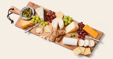 Kaasplank met verschillende soorten kazen, druiven, crackers, augurken en noten, geserveerd op een houten plank.