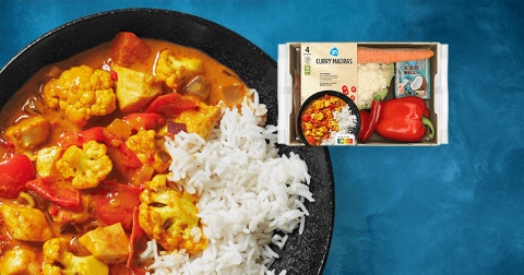 AH Curry Madras maaltijdpakket met een bord rijst, curry met groenten zoals bloemkool en paprika op een blauwe achtergrond