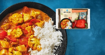 AH Curry Madras maaltijdpakket met een bord rijst, curry met groenten zoals bloemkool en paprika op een blauwe achtergrond