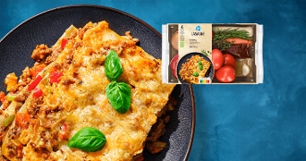 Lasagne op een bord, gegarneerd met verse basilicum, met daarboven de verpakking van de Albert Heijn lasagne maaltijd