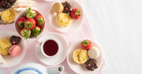 Theetafel met verschillende zoete en hartige hapjes, waaronder aardbeien, macaron, chocoladekoekjes, quiches en een kopje thee.