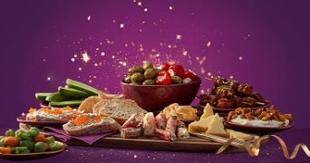 Feestelijke borrelplank met diverse hapjes zoals gevulde olijven, kaas, vleeswaren, toastjes met luxe toppings en groente, gepresenteerd op een paarse achtergrond met sprankelende lichteffecten