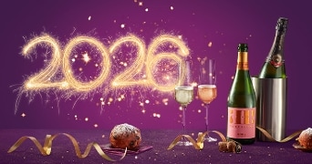 Feestelijke nieuwjaarssetting met knallende 2026 van sterretjes, twee glazen mousserende wijn, een fles Cava, een fles mousserende wijn in een koeler, oliebollen en gouden slinger op een paarse achtergrond
