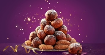 Stapel oliebollen en appelbeignets op een schaal met feestelijke paarse achtergrond