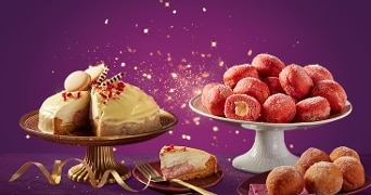 Feestelijke presentatie van een taart met witte chocoladeglazuur en macarons, naast een schaal met roze gevulde oliebollen, op een paarse feestelijke achtergrond