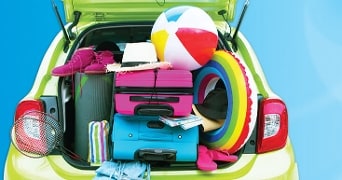 Groene kofferbak vol met vakantiespullen, inclusief gekleurde koffers, een strandbal en een opblaasbare zwemband.